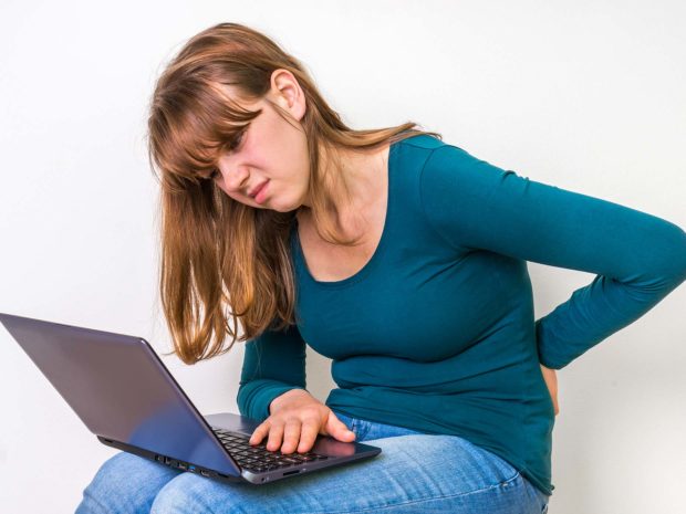 ragazzina si tocca a schiena dolorante con sulle ginocchia il computer