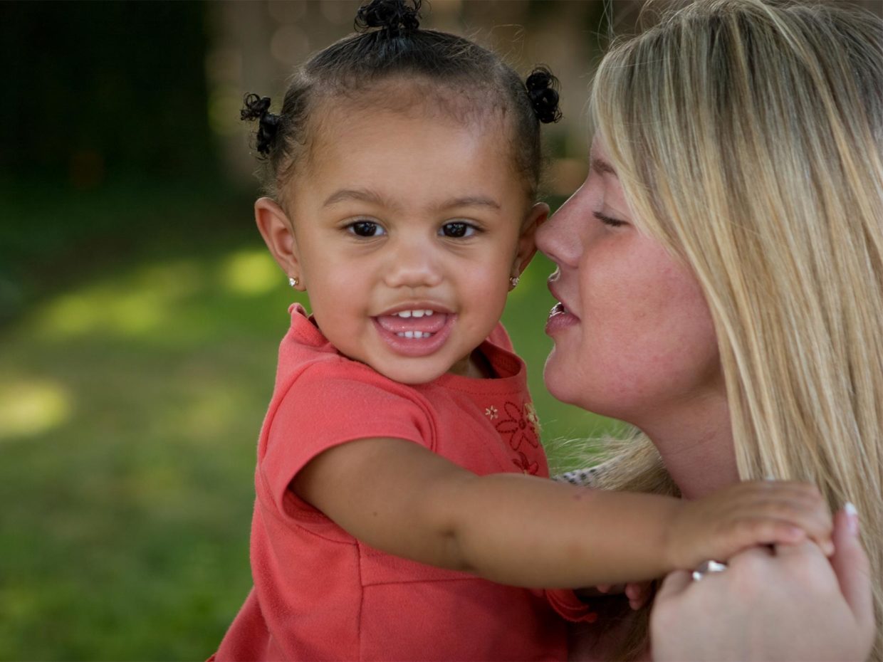 bambina di colore in braccio alla madre adottiva