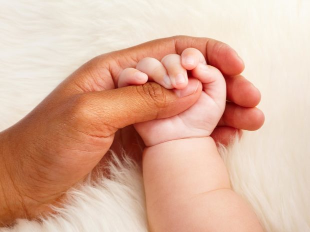 mano di una mamma di diversa etnia tiene la mano di un neonato