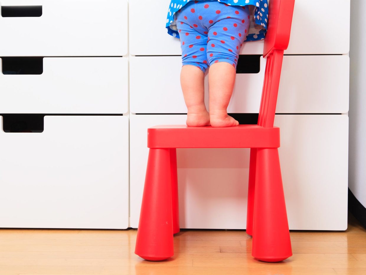 bambina piccola in piedi su una sedia di plastica rossa