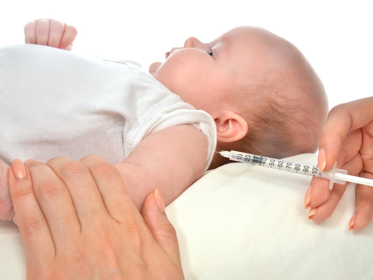 neonato disteso con braccio tenuto fermo per la vaccinazione