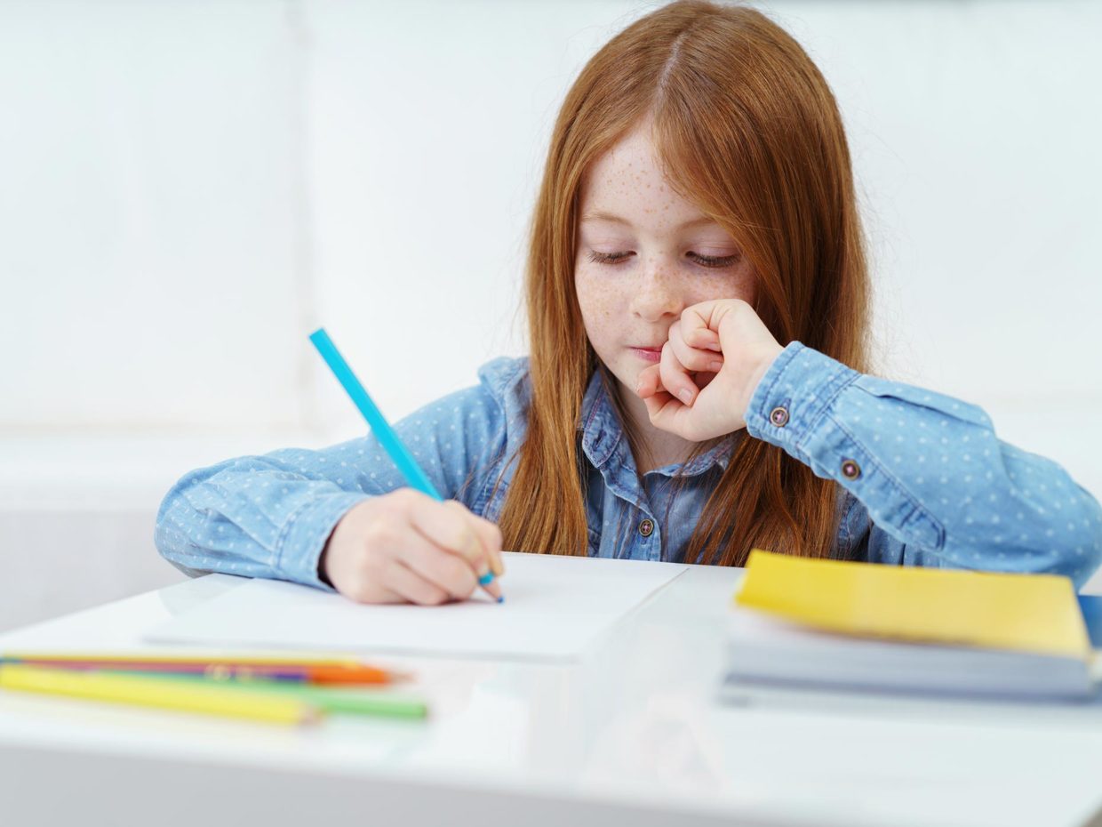 bambina con i capelli rossi impegnata a fare i compiti
