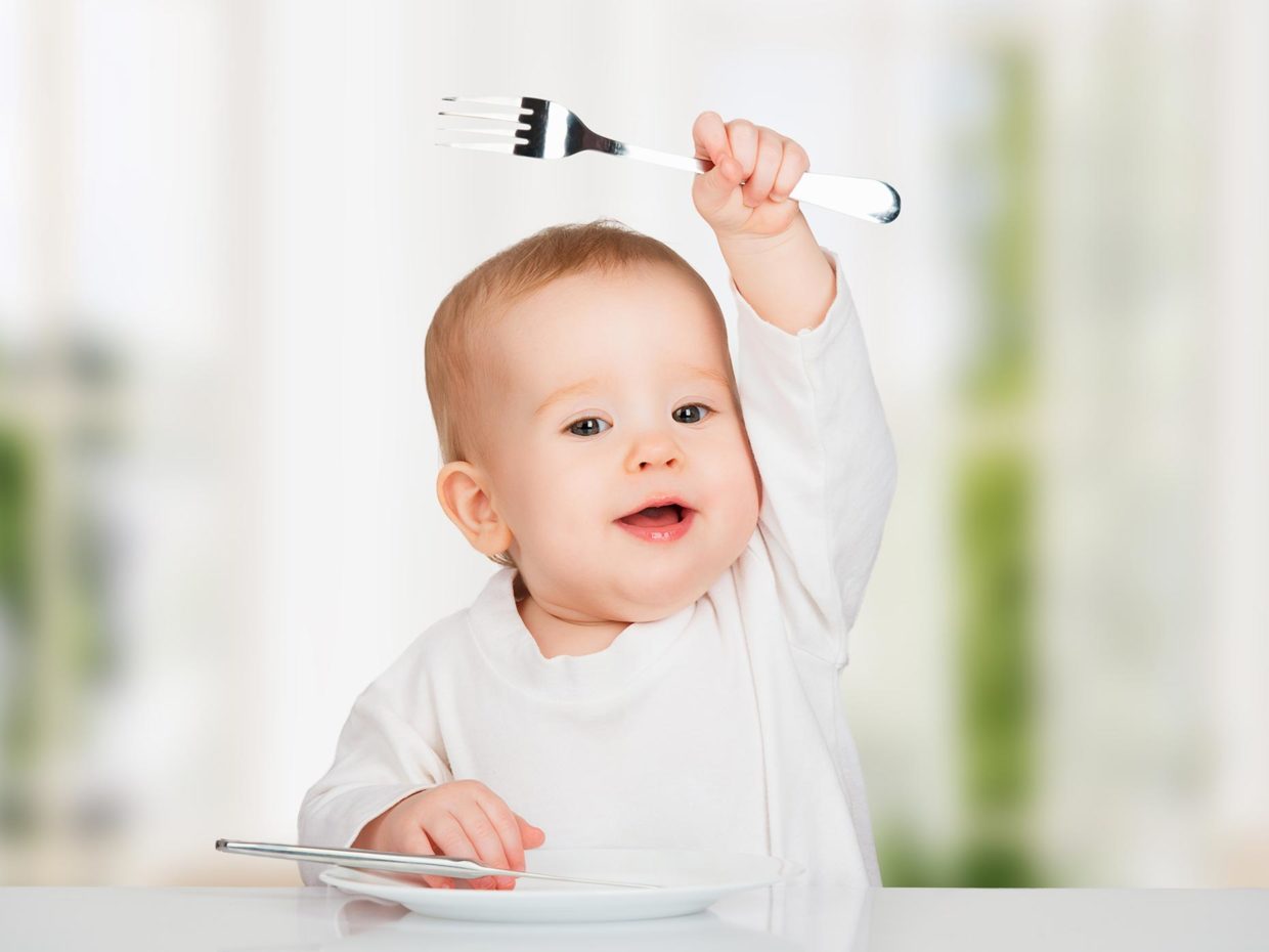 bambino piccolo solleva il braccio con in mano una forchetta