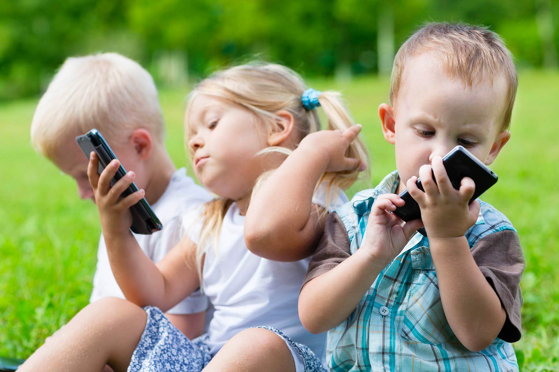 tre bambini piccoli usano lo smartphone