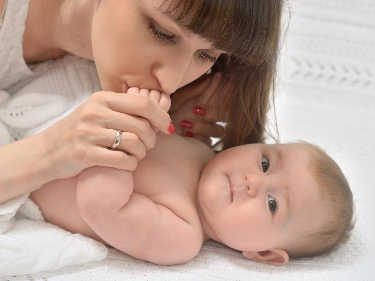 neonato coccolato dalla mamma che gli bacia la mano
