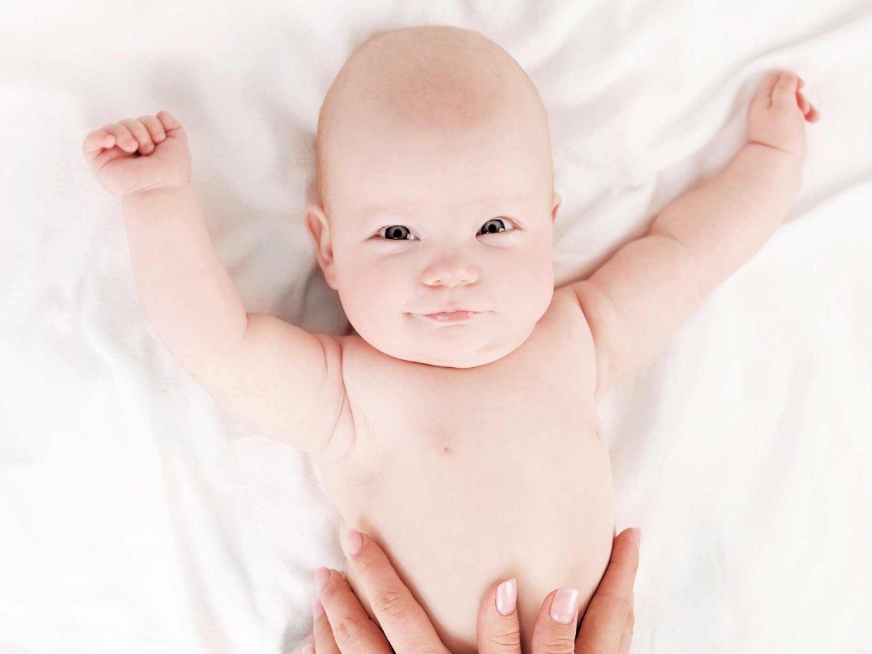 neonato disteso nel letto con le braccia aperte viene massaggiato dal genitore