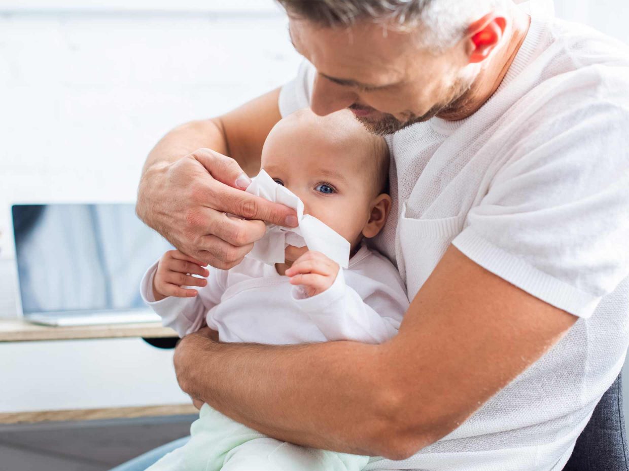 papà pulisce il naso del figlio neonato tenendolo in braccio