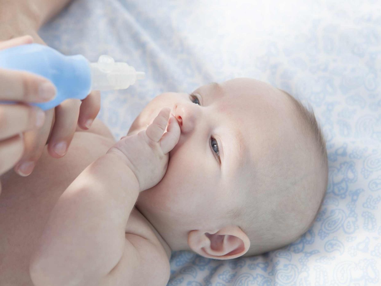 neonato disteso in un letto osserva l'aspiratore nasale a pompetta tenuto in mano dal genitore