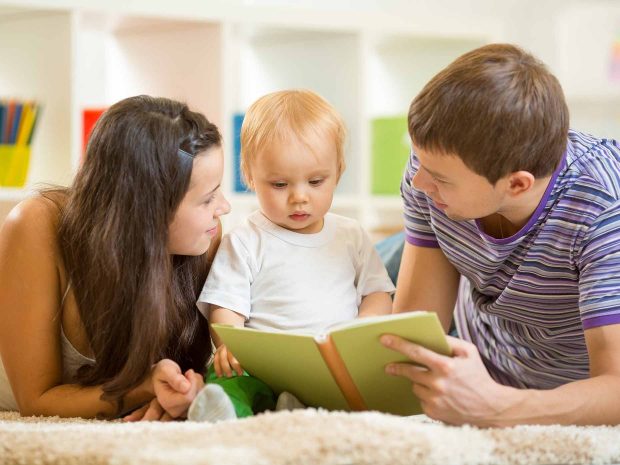 mamma e papà distesi sul tappeto leggono libro al figlio piccolo